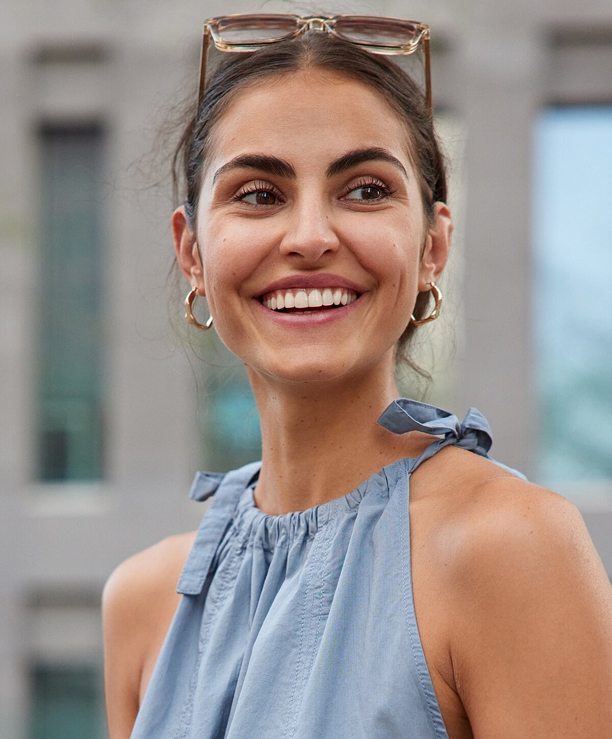 Smiling woman in blue sleeveless top outdoors.