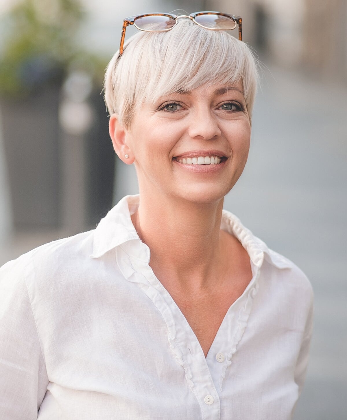 Smiling woman with short blond hair outdoors.