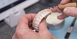 Dental technician sculpting a denture model.