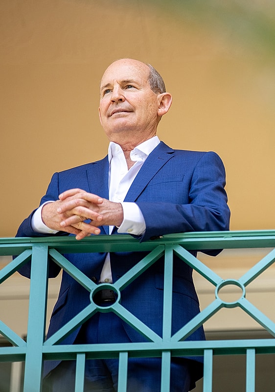 Man in suit standing on balcony, arms crossed.