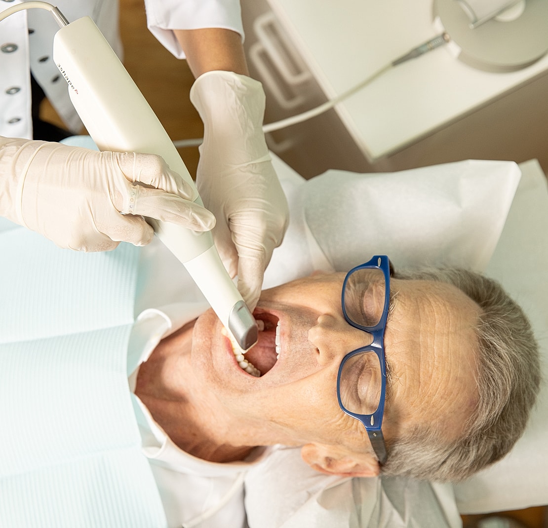 Dentist using scanner on patient’s open mouth.