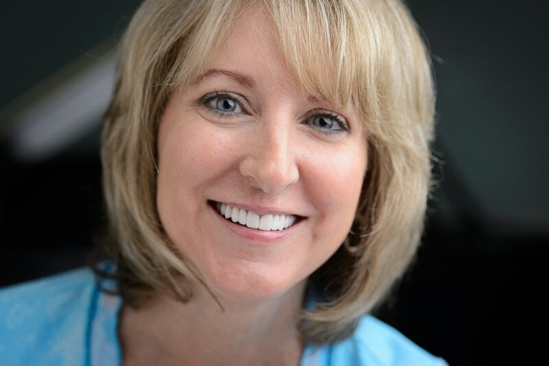 Smiling woman with blonde hair and blue shirt.