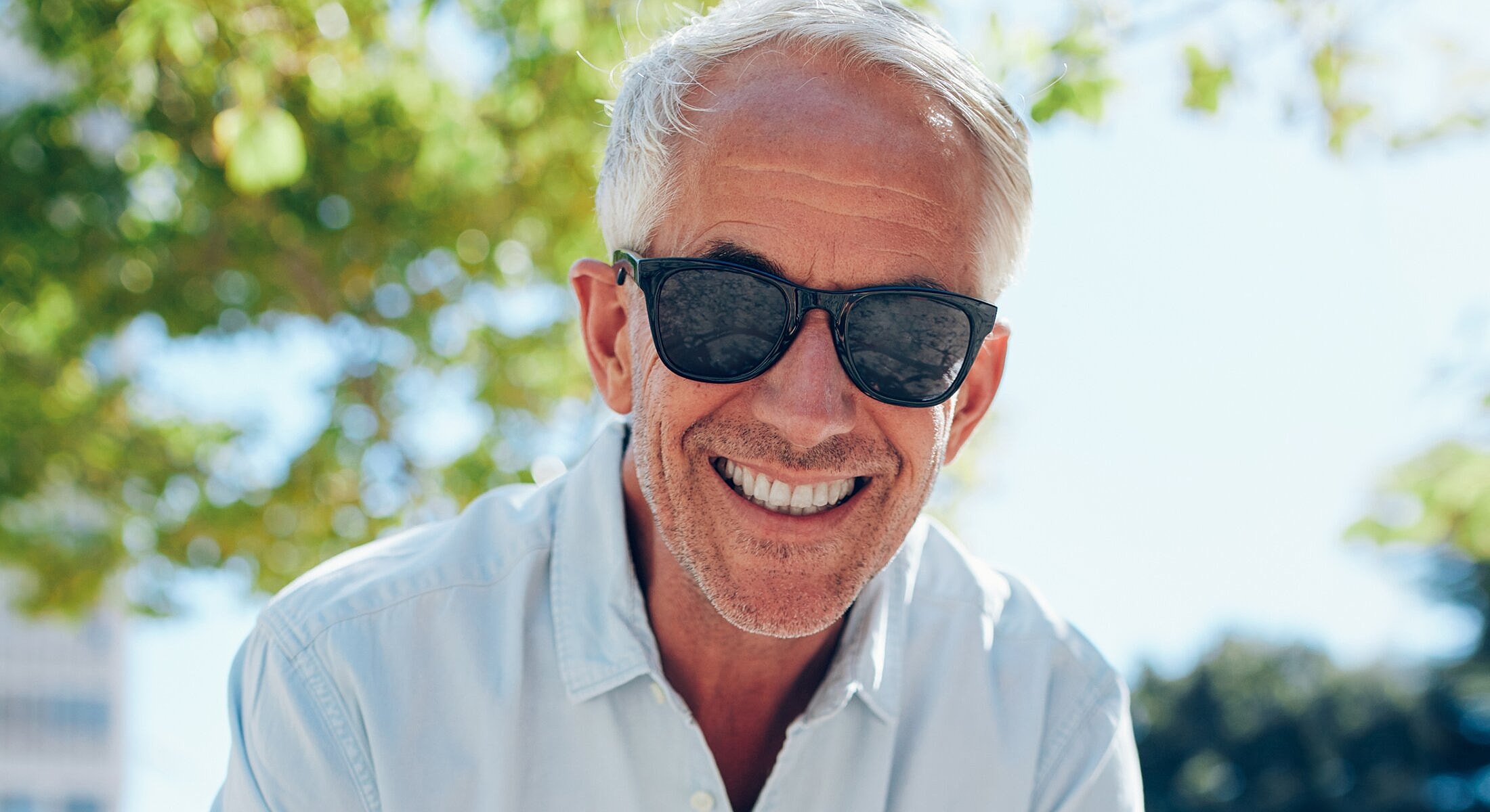 Smiling older man wearing sunglasses outdoors.