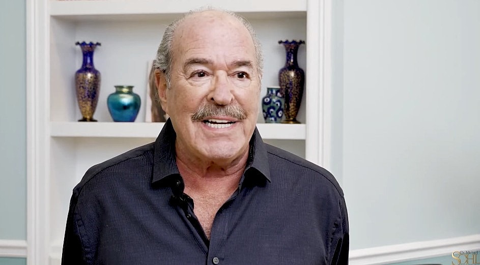 Man in a cowboy hat smiling warmly indoors.